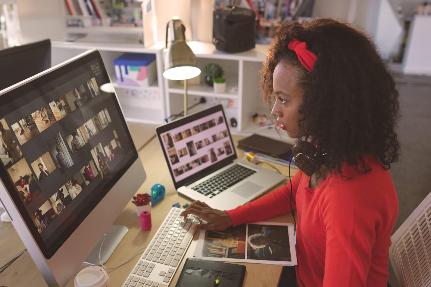A person drawing on a graphic tablet at desk while looking at image gallery on desktop screen and secondary laptop. Creative and Interactive Design