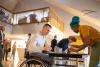 A person in a wheelchair signing in at a conference registration table while conference specialist prepares his badge and conference program.